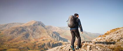 A lone make hiker with backpack walks away from the camera and toward the Welsh mountains.